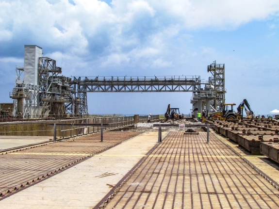 Large-format photograph: Pad Deck, Launch Complex 39-B, showing Apollo Era Crawlerway Grid Panels east of the Flame Trench in the area just south of the Catacombs Roof, where the Panels are divided into two runs, one each for both of the Crawler Trackways. In the distance, the North Piping Bridge, for which Sheffield Steel was extorted by NASA Contracting Management to the tune of $200,000 dollars in exchange for being allowed to leave it in place, as-fabricated, following a horseshit dispute over a fabrication ”discrepancy,” can be seen spanning the Flame Trench, still standing, no problem, all these years later, despite the ”discrepancy” having never been touched or altered in any way. Photo credit: Withheld by request. Photo credit: Withheld by request.